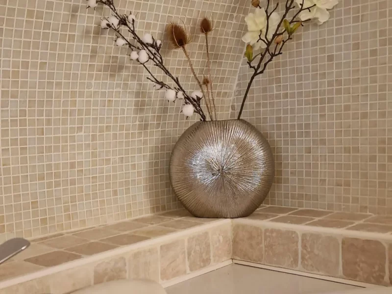 Vase rond contenant des fleurs séchées dans un coin de mur en mosaïques